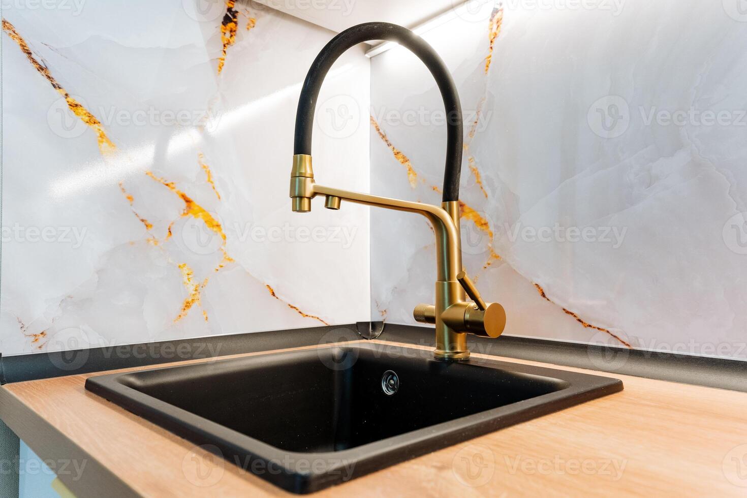 In a beautifully designed kitchen, there is a sleek black sink that perfectly complements a stunning gold faucet, creating an elegant and modern aesthetic in this household setting photo