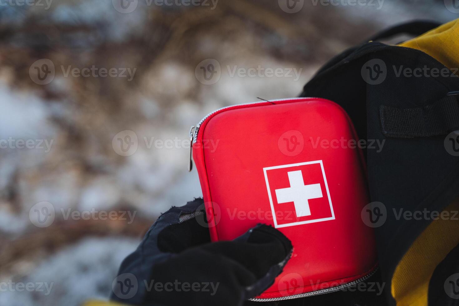 A person is firmly holding a brightly colored red first aid kit that features a distinctive white cross symbol, making it easily identifiable during emergencies for quick access photo