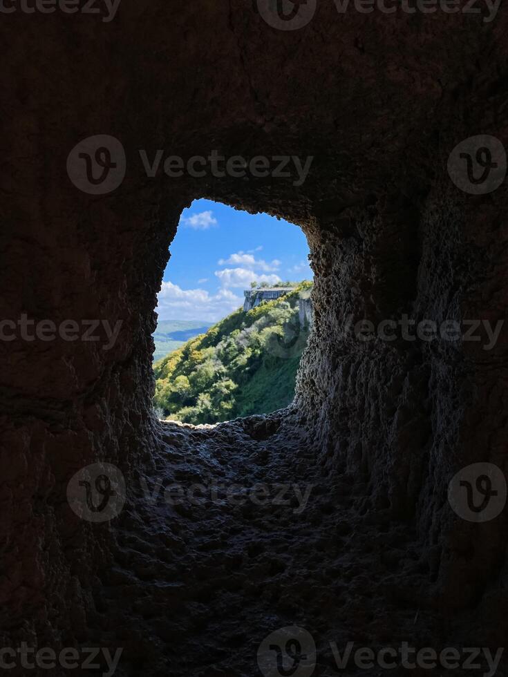 An exquisite view of an expansive landscape can be seen through a unique hole in a rock wall, showcasing the beauty of natures geological formations and the effects of erosion photo