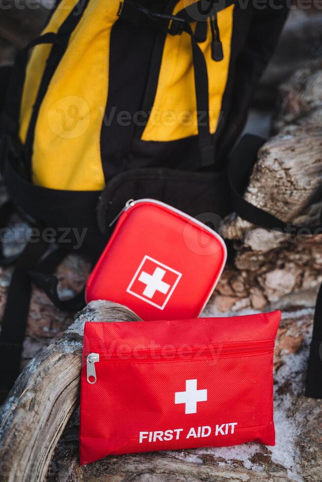 A first aid kit is crucial for managing emergencies and is conveniently placed on a rock next to a backpack, which likely holds additional vital items needed for outdoor activities photo