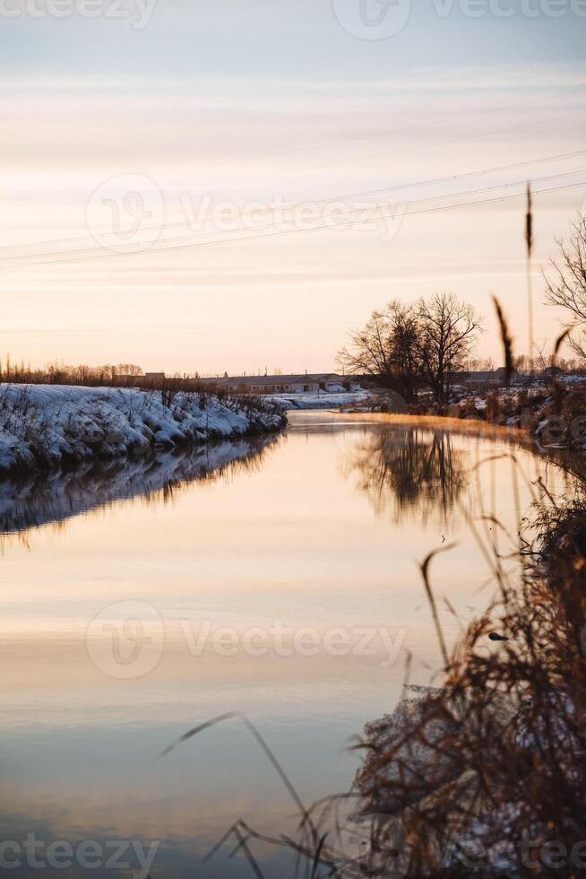 A serene river flowing gently, framed by lush trees along the shore, with a beautiful bridge gracefully arching in the background, all illuminated by the warm hues of sunset photo