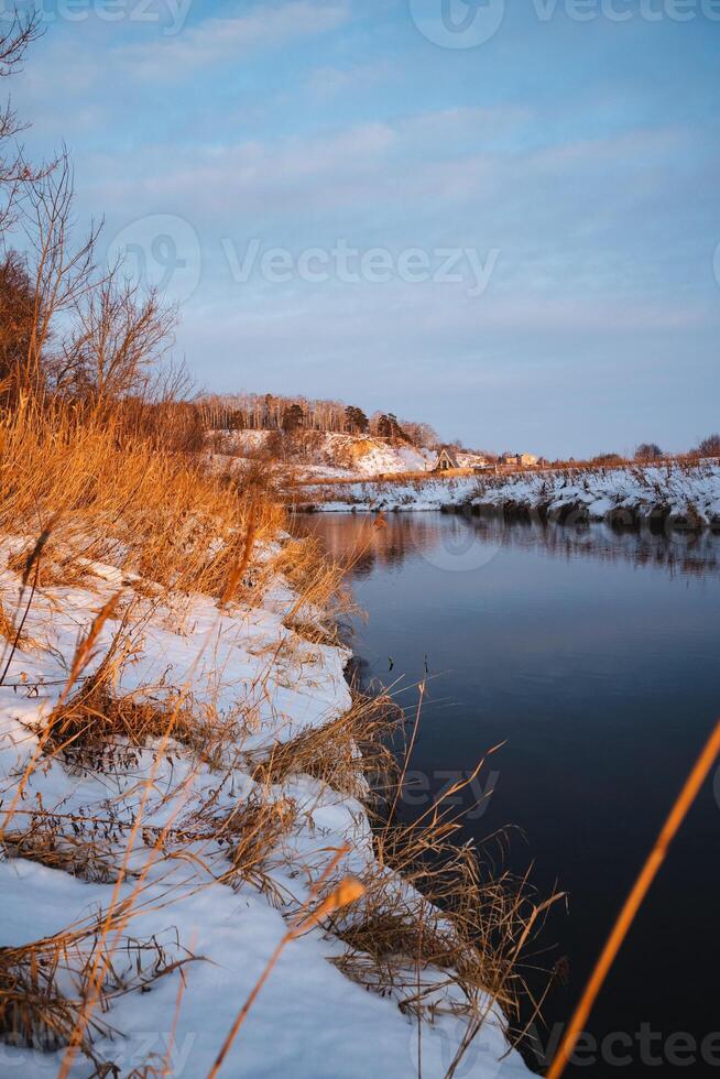 A picturesque snowy shoreline of a serene river, with a fishing rod prominently placed in the foreground, creating a charming winter scene that captures the essence of natures beauty photo