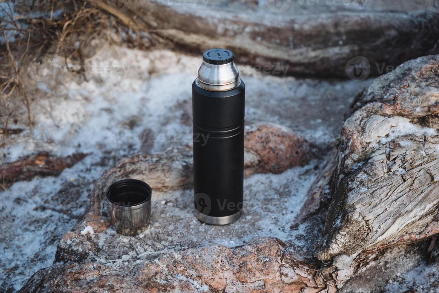 A sleek, stylish black thermos featuring a modern design elegantly rests upon beautifully sculpted rocks, perfectly showcasing its sophisticated appearance against a rugged natural backdrop photo