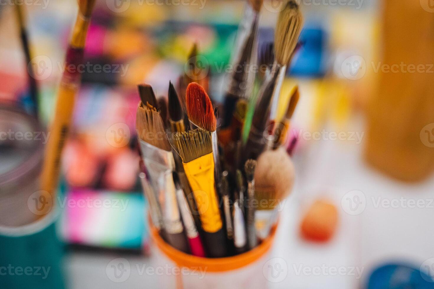 A collection of various paint brushes is placed neatly in a cup, which sits atop a table, showcasing the colorful tools ready for creative use in art projects or other applications photo