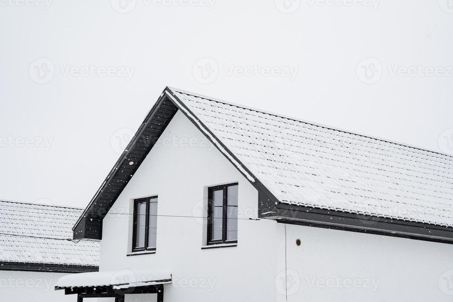 A charming white house adorned with a striking black roof is completely blanketed in soft, fluffy snow, creating a picturesque winter scene that captures the essence of the season photo