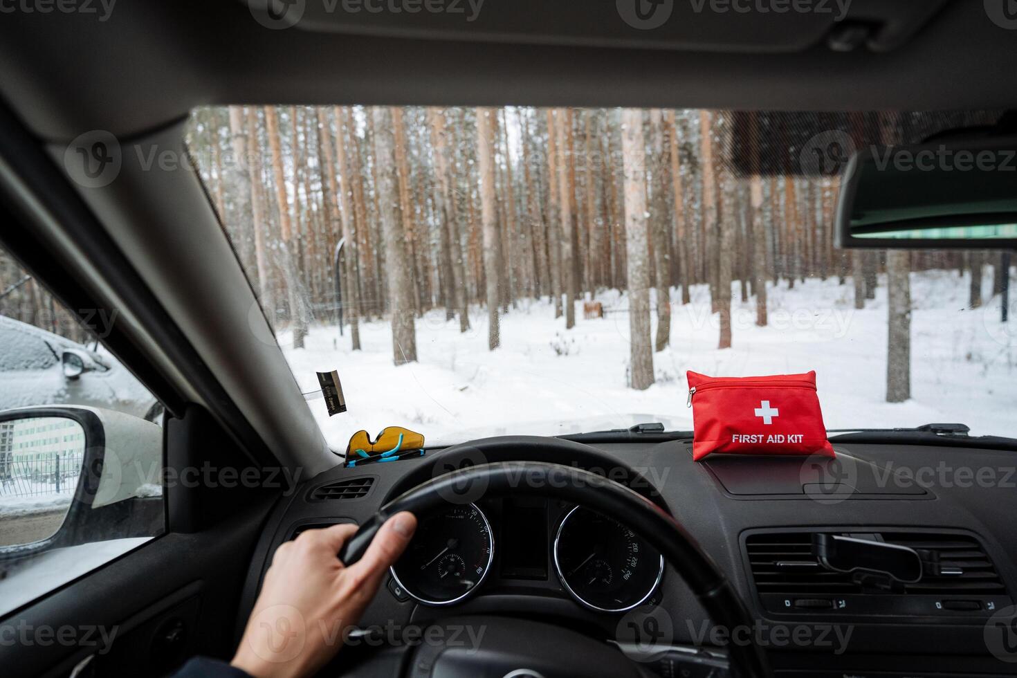 A person is actively driving a car, and there is a first aid kit conveniently placed on the dashboard for quick access in case of any emergencies that may arise during the trip photo