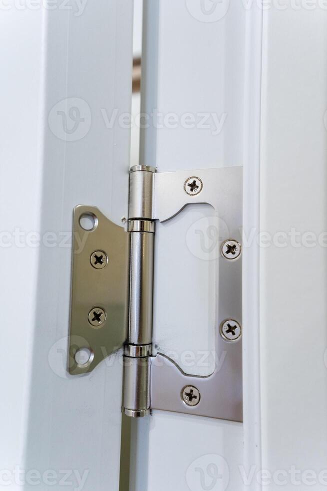 This is a closeup view of a stainless steel door hinge attached to a contemporary white door frame, showcasing its sleek design and functionality photo