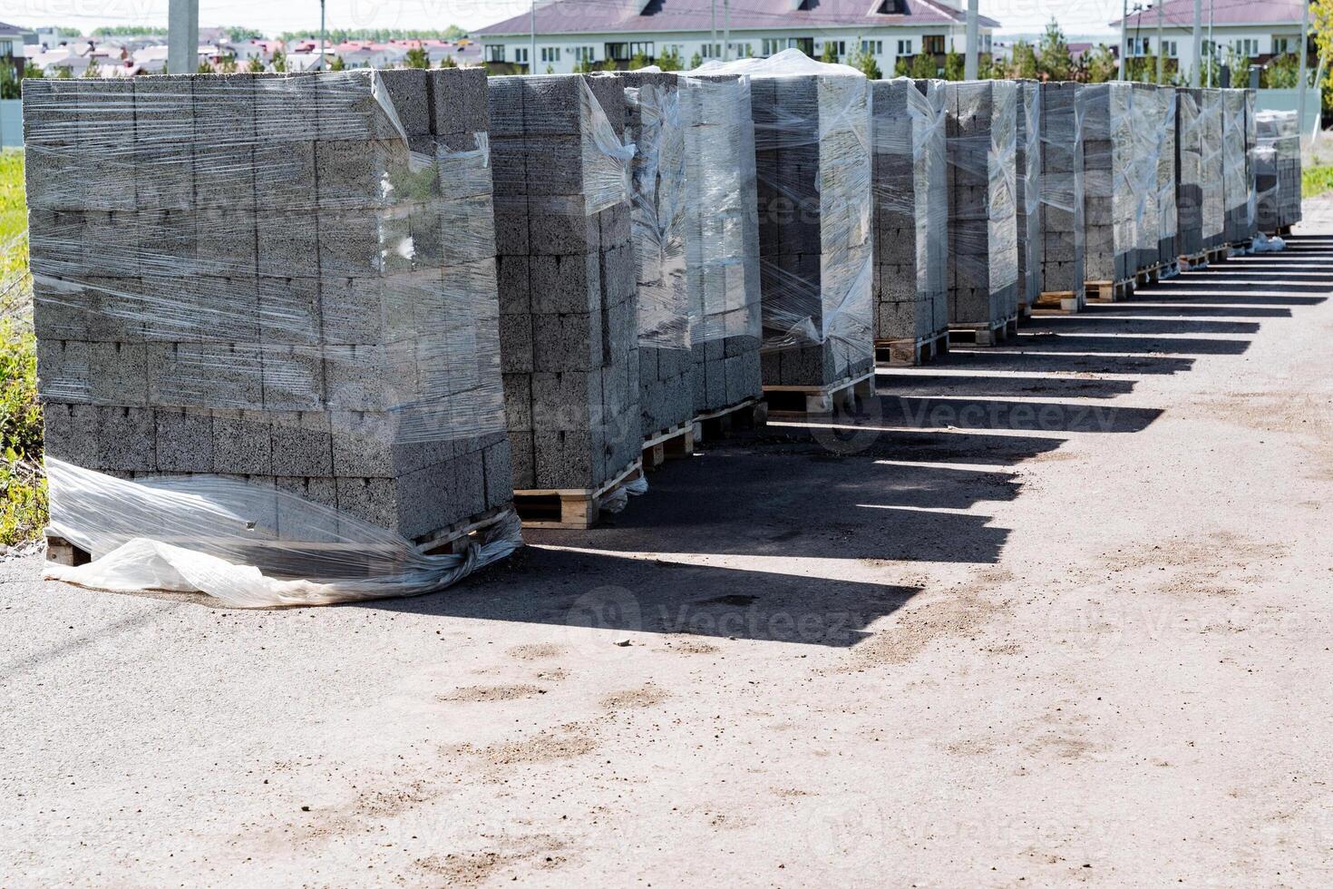 Pallets of neatly arranged concrete paving blocks at construction site for new building development, outdoor storage of heavy materials, wrapped in microwave wrap for future housing project photo