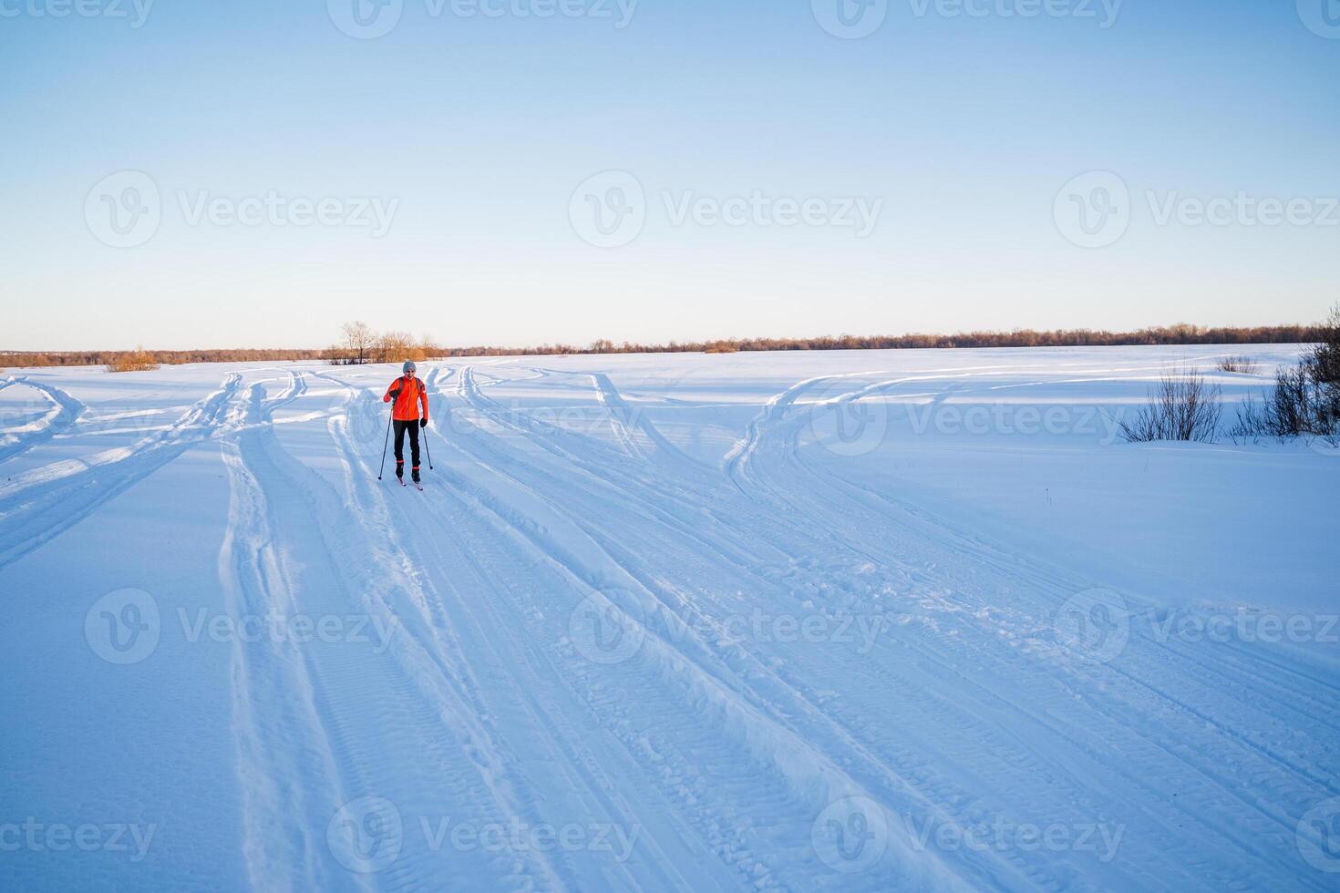 In the distance, a skier in a red suit is running, a man is skiing on a snowy field. photo