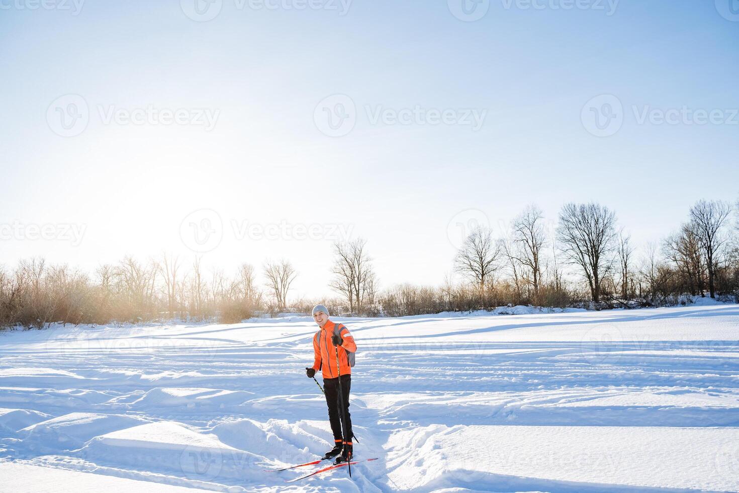 Skier standing on the snow against the background of the glare of the sun, training in the winter forest, sports and recreation. photo