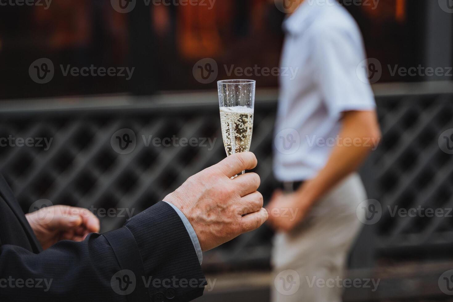 Man gesturing with glass of champagne at another man at event photo