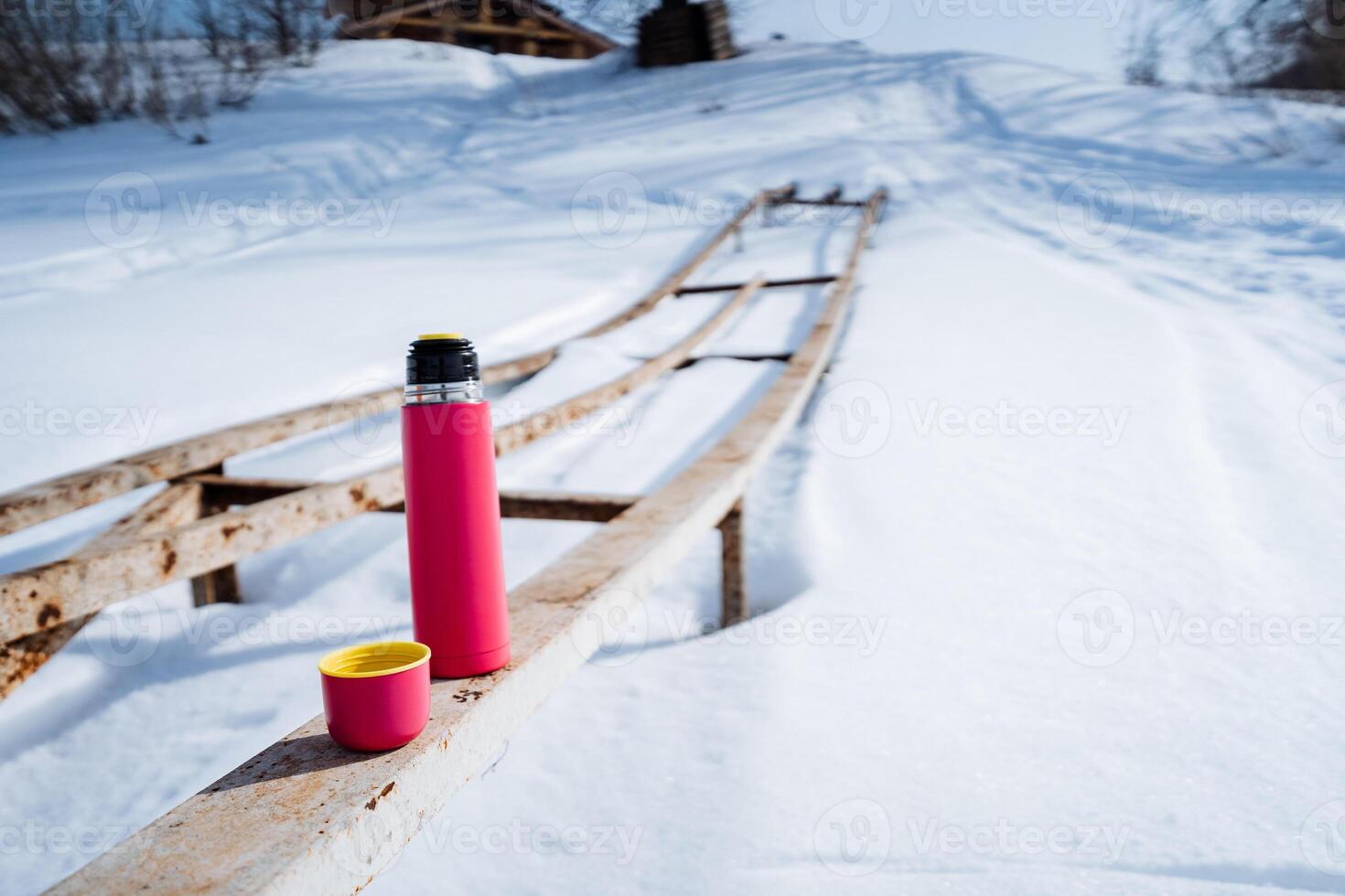 A pink thermos and cup rest on a wooden bench in the freezing snow photo