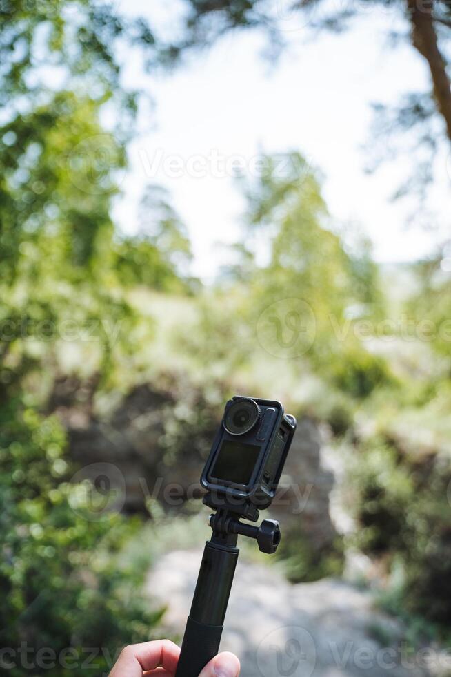 A person is calmly taking pictures in a serene natural environment with a camera securely placed on a tripod. The beautiful scenery consists of trees, grass, and lovely views photo