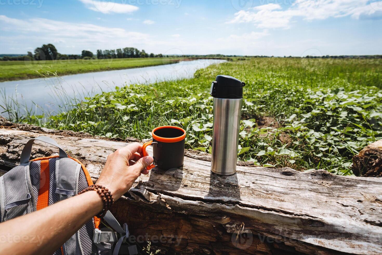 picnic in nature, there is a thermos and a mug on a tree, tourist utensils made of metal, drink hot tea in the forest, summer heat in nature. photo