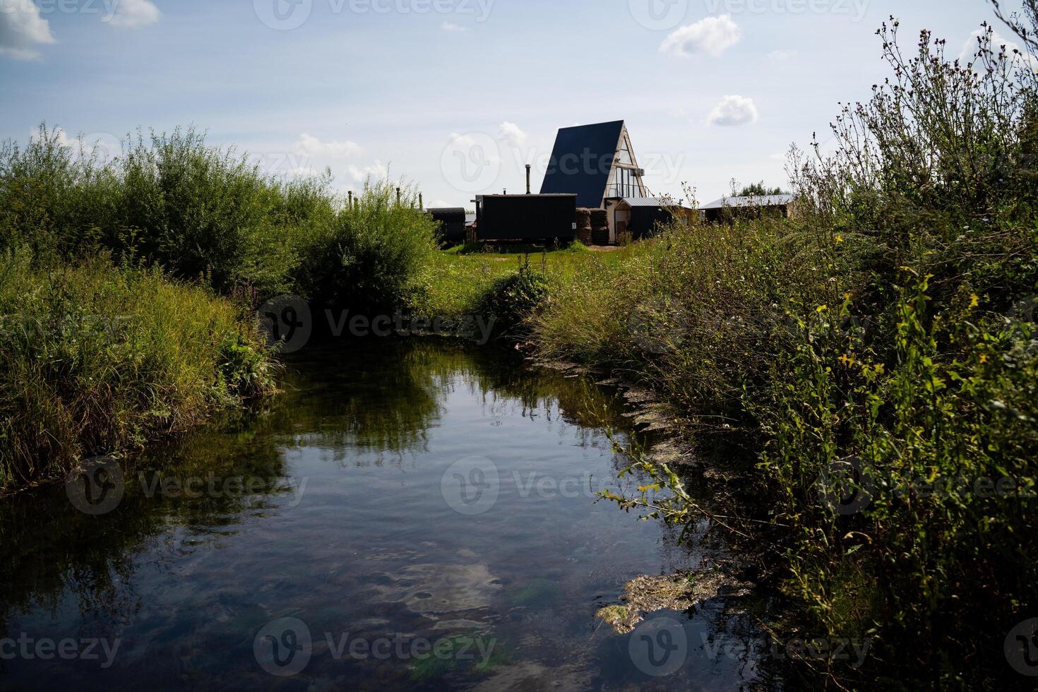 In the picturesque scene, a small, tranquil river flows gently along, with a charming house nestled in the background, creating a serene and inviting atmosphere in nature photo