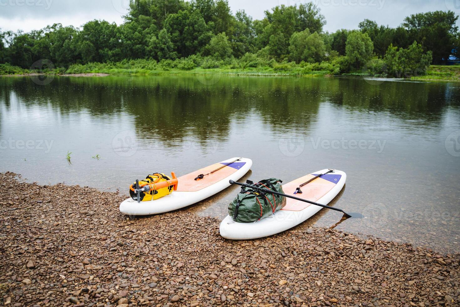 Two paddleboards are placed along the shore in preparation for a river journey. The peaceful setting encourages relaxation and exploration amidst lush greenery photo