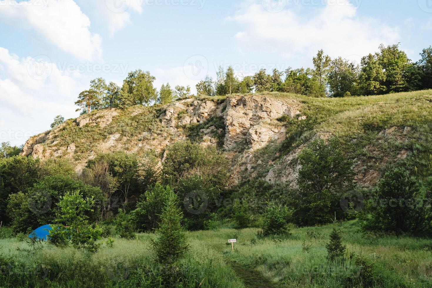 Tent hidden in the grass among the trees against the background of a rock, tourist parking in the forest, camping in nature, mountain peak, early morning. photo