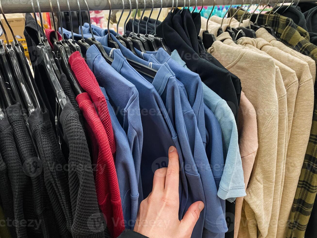 A person is thoughtfully selecting a stylish and fashionable shirt from a wellorganized rack in a trendy fashion store, in search of the ideal piece to enhance and elevate their wardrobe photo