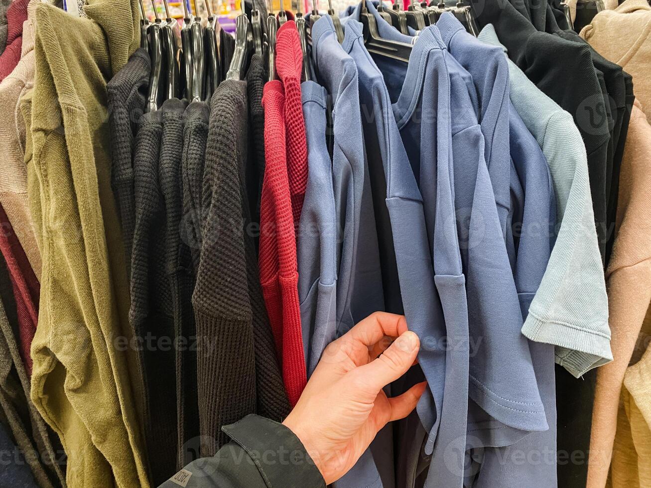 A person is currently holding a stylish blue shirt in front of a diverse rack filled with various clothes and garments, showcasing a variety of fashion choices available for selection photo