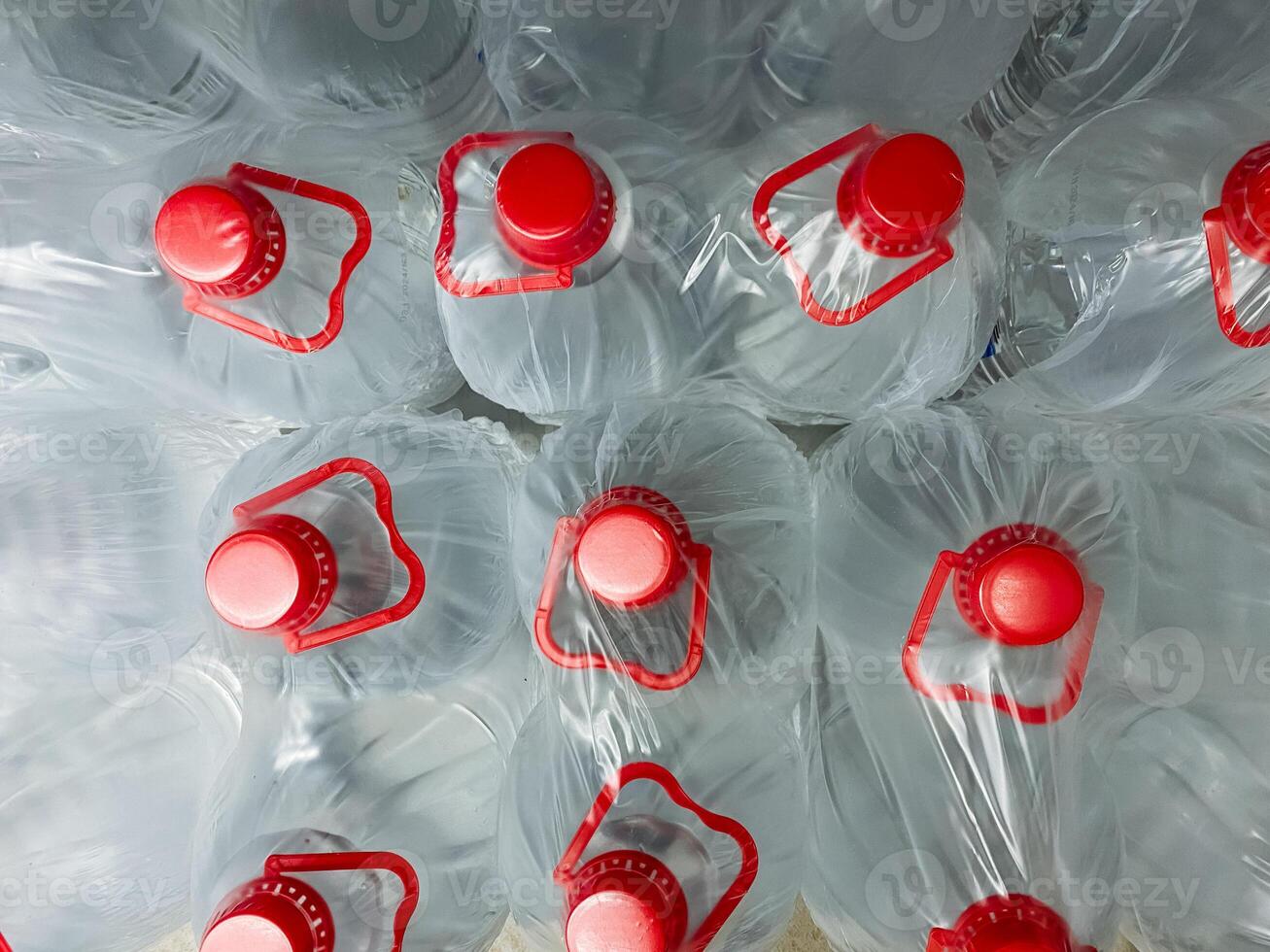There is a significant stack of plastic water bottles, each adorned with red caps that make them easily recognizable, perfect for holding fluid or liquid like water for drinking photo