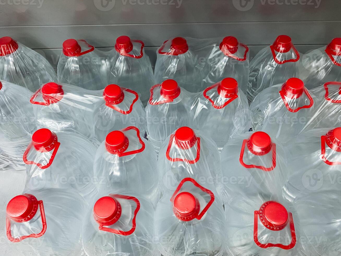 A large stack of assorted plastic water bottles that each have vibrant red caps is neatly arranged on top of one another, showcasing the colorful plastic design and structure of these items photo