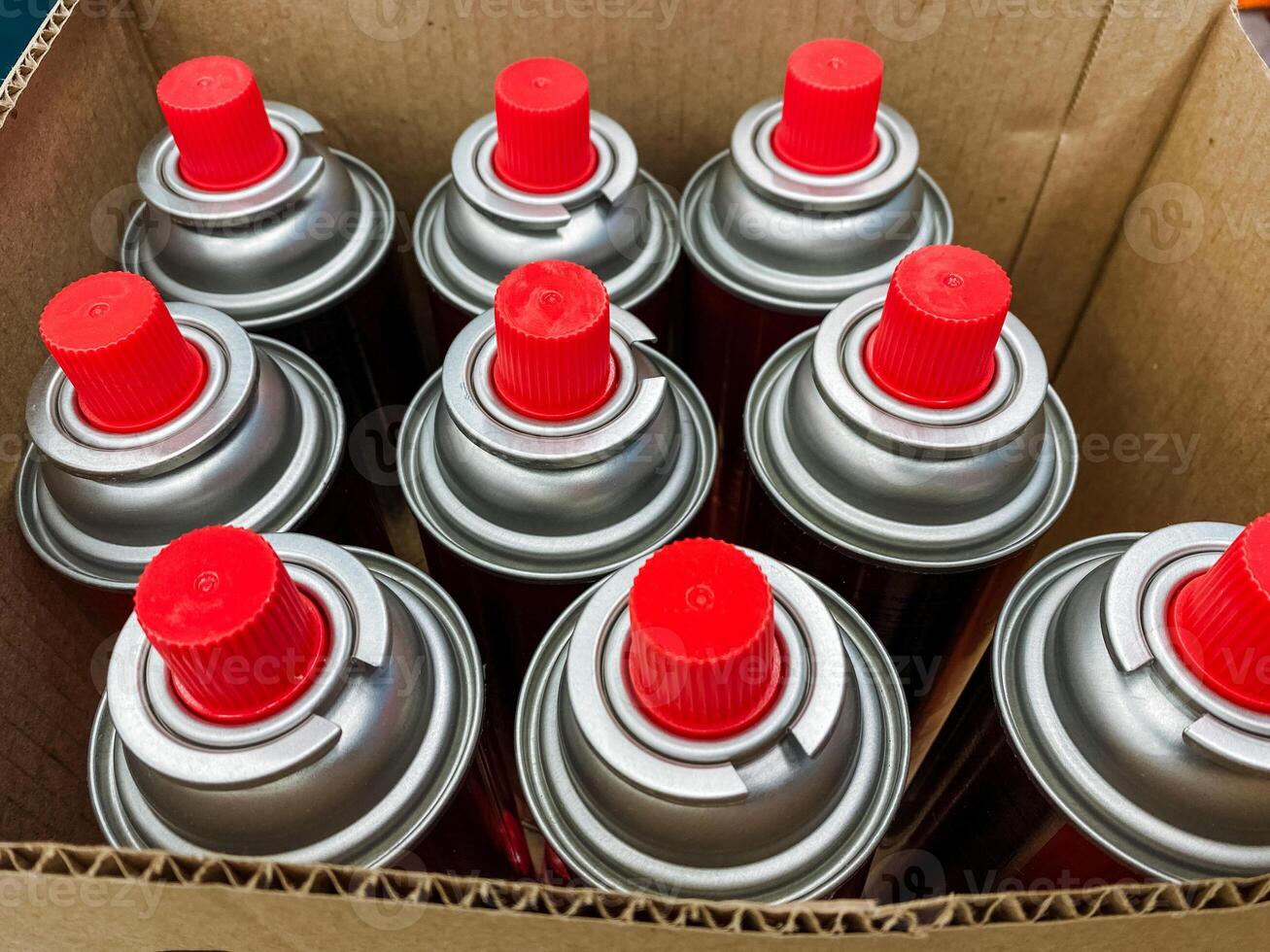 A large cardboard box filled to the brim with a variety of colorful spray cans, all featuring bright red caps that stand out prominently against the materials of the box photo