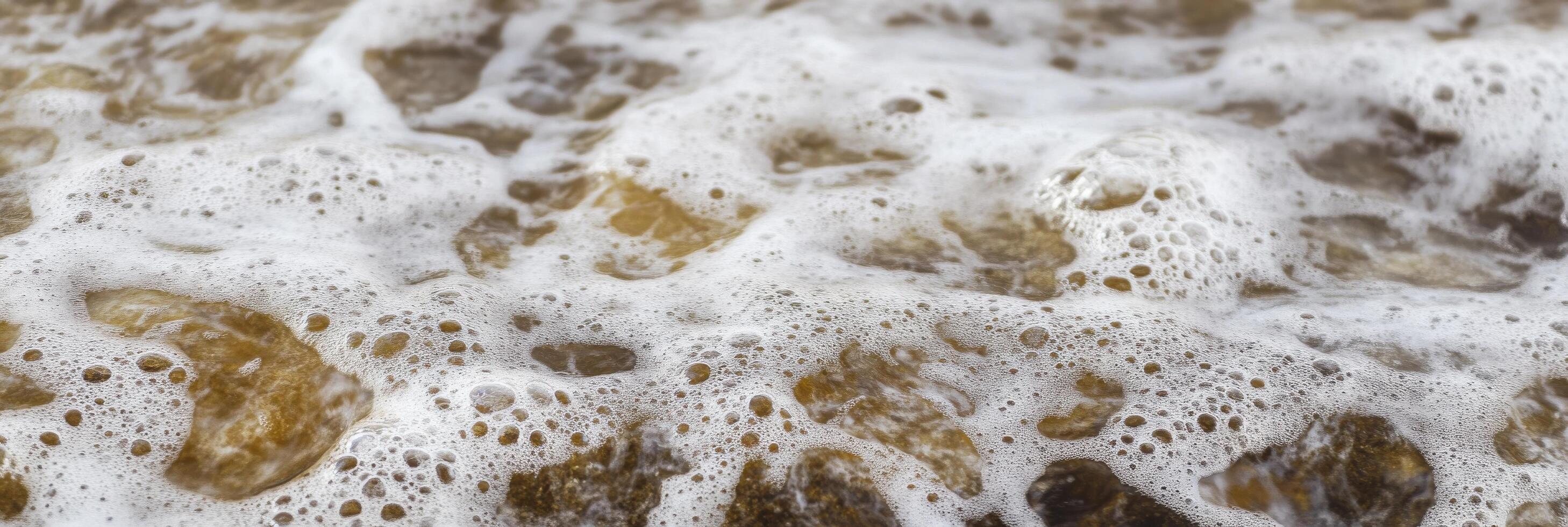 Close-up view of sea foam and bubbles forming over brown pebbles near shore photo