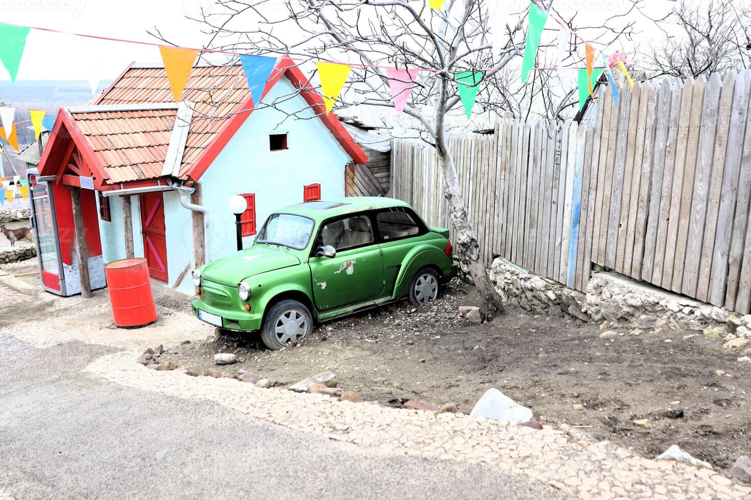 A Charming Green Car Parked Right Next to a Colorful Miniature House in a Scenic Setting photo