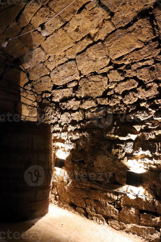 An inviting, rustic stone wall paired with an aged barrel in a dimly lit, charming cellar photo