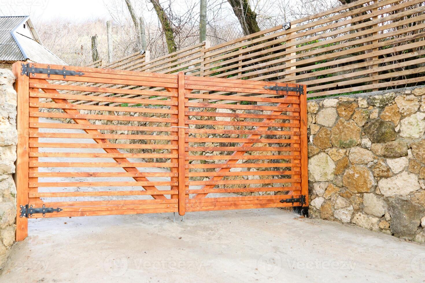 An Elegant and Stylish Wooden Gate Framed by a Stone Wall and Complemented by a Slatted Fence photo