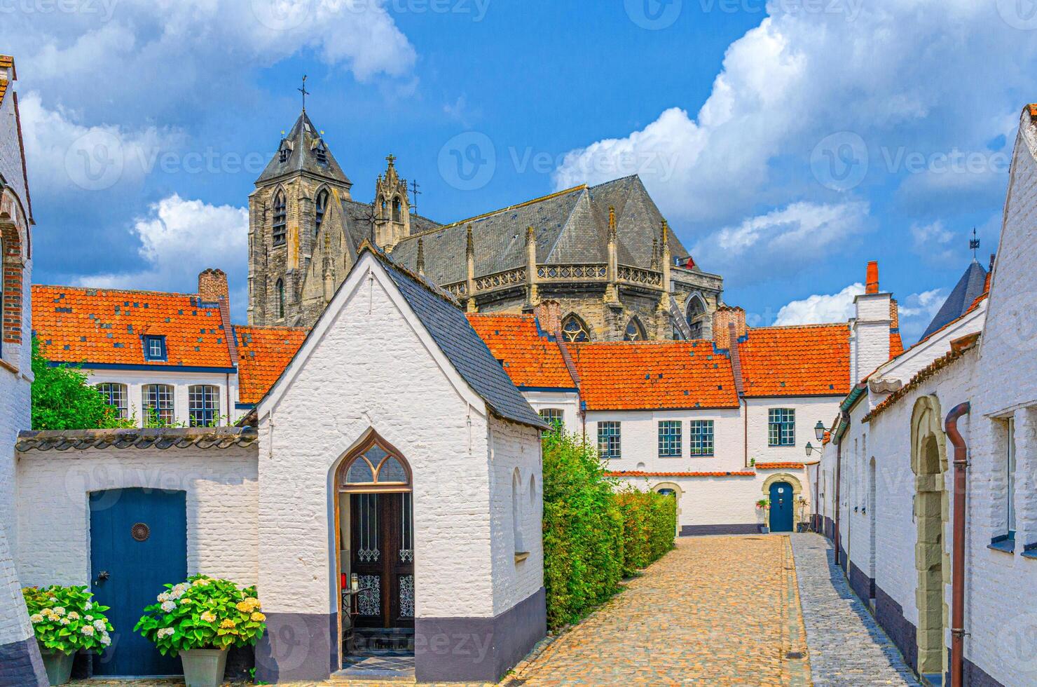 Beguinage Courtrai, Begijnhof van Kortrijk with white houses on narrow cobblestone street in historical city centre, Church of Our Lady background, Flemish Beguinages, West Flanders province, Belgium photo