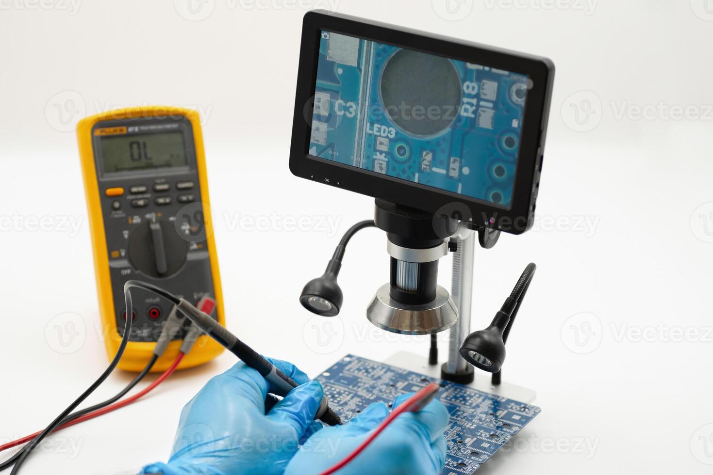 Closeup examination of a circuit board using a digital microscope and multimeter in a workshop photo