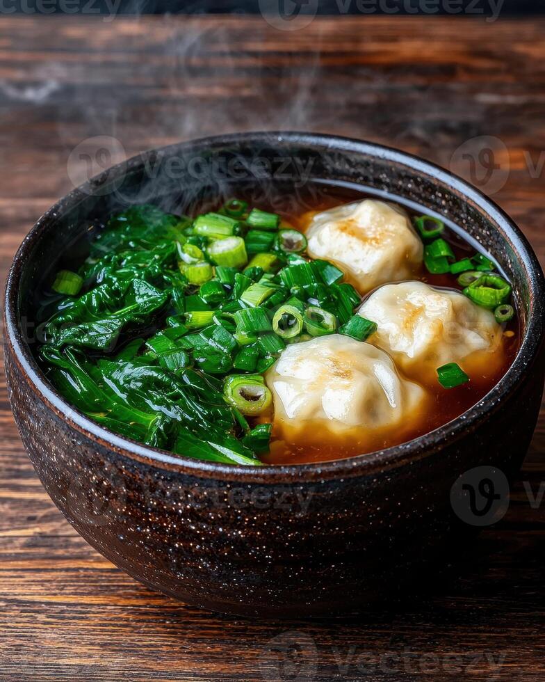 Steaming bowl of wonton soup with spinach and green onions photo
