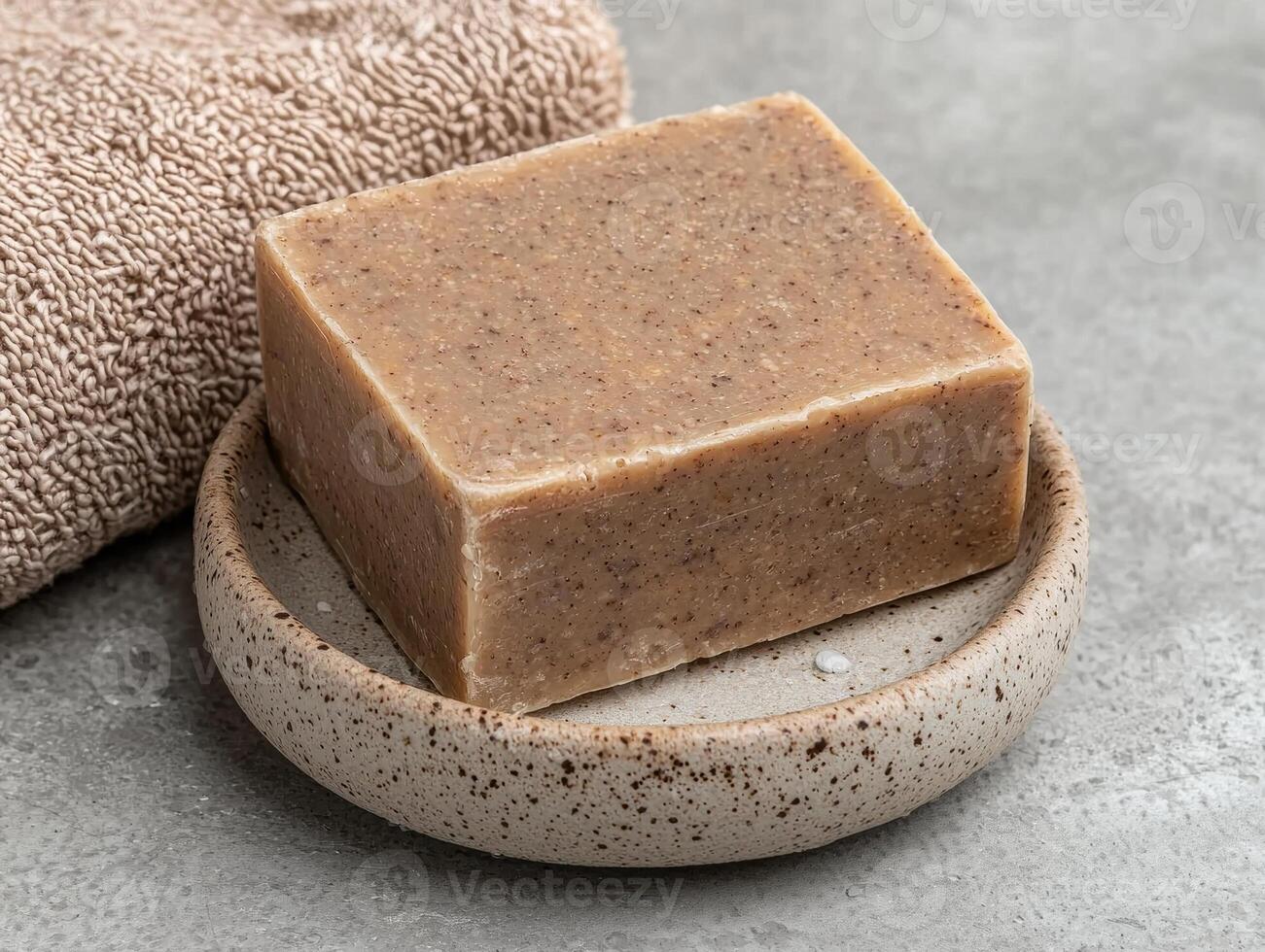 A bar of natural soap sits on a rustic soap dish next to a towel photo