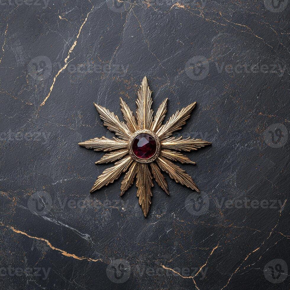 Gold starburst brooch with dark red gemstone on dark marble background photo