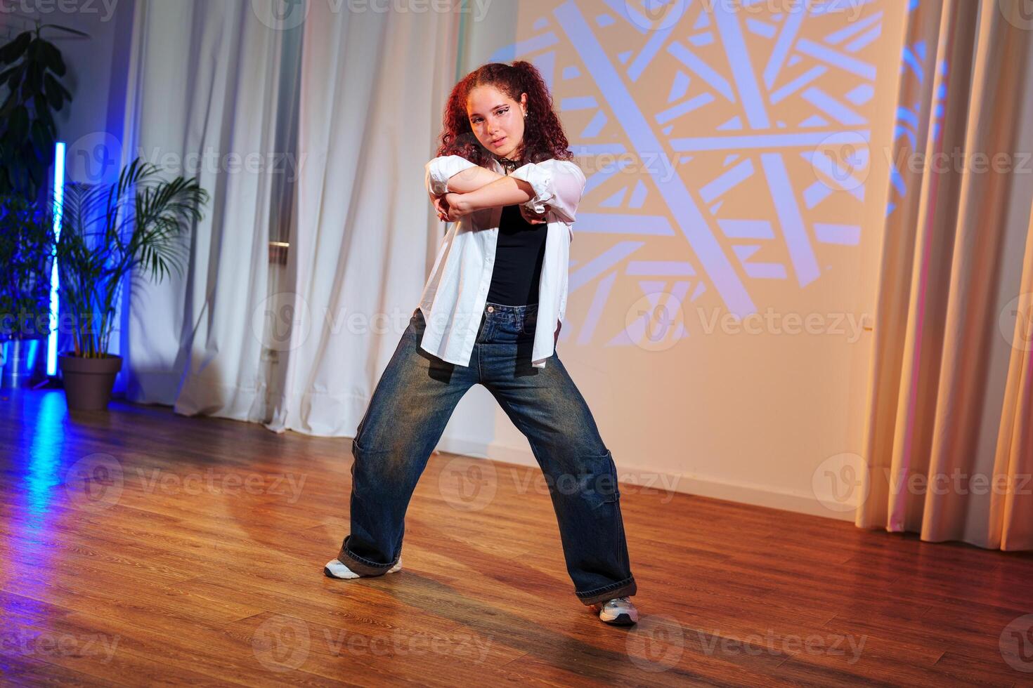 A woman in a white shirt and blue jeans dances in a studio with a blue light shining on the floor photo
