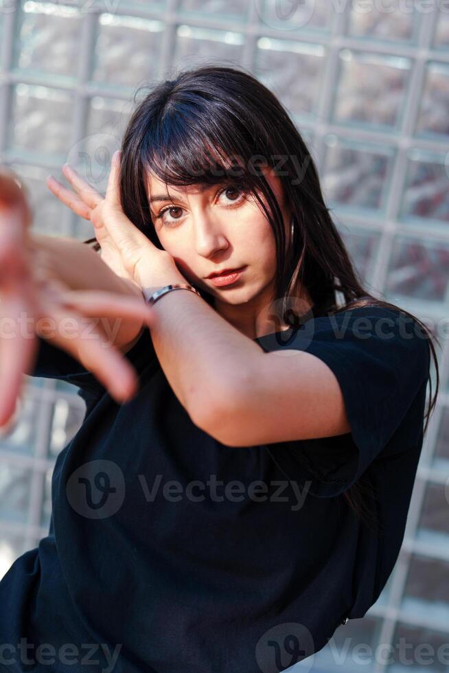 Young woman poses dramatically in front of patterned glass wall during artistic photo shoot in urban setting