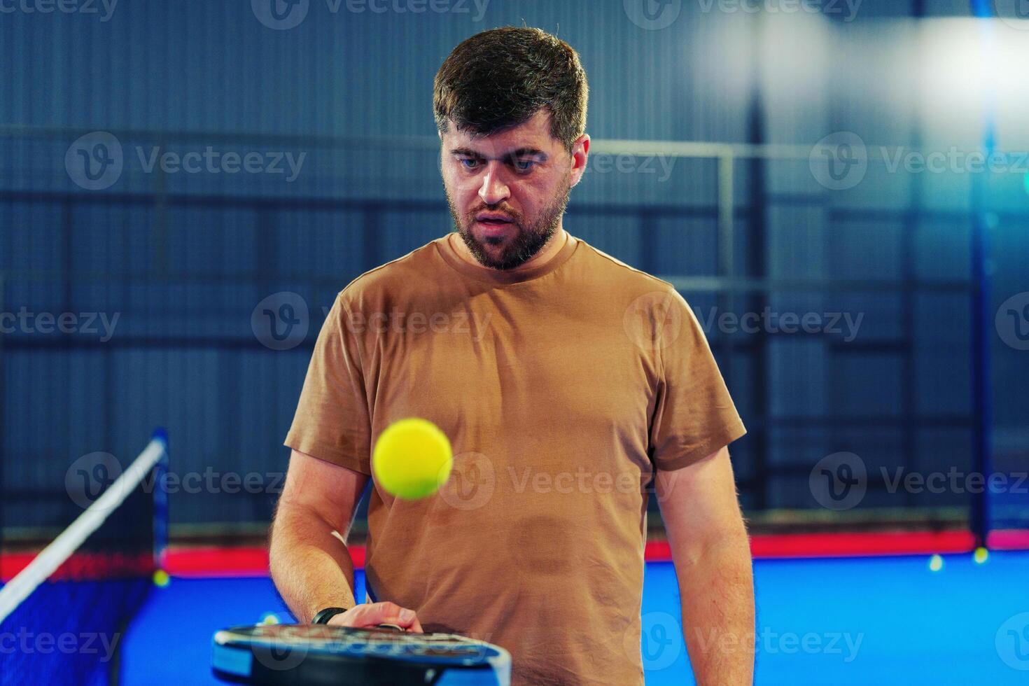 Man practicing tennis skills with a yellow ball in an indoor court setting photo