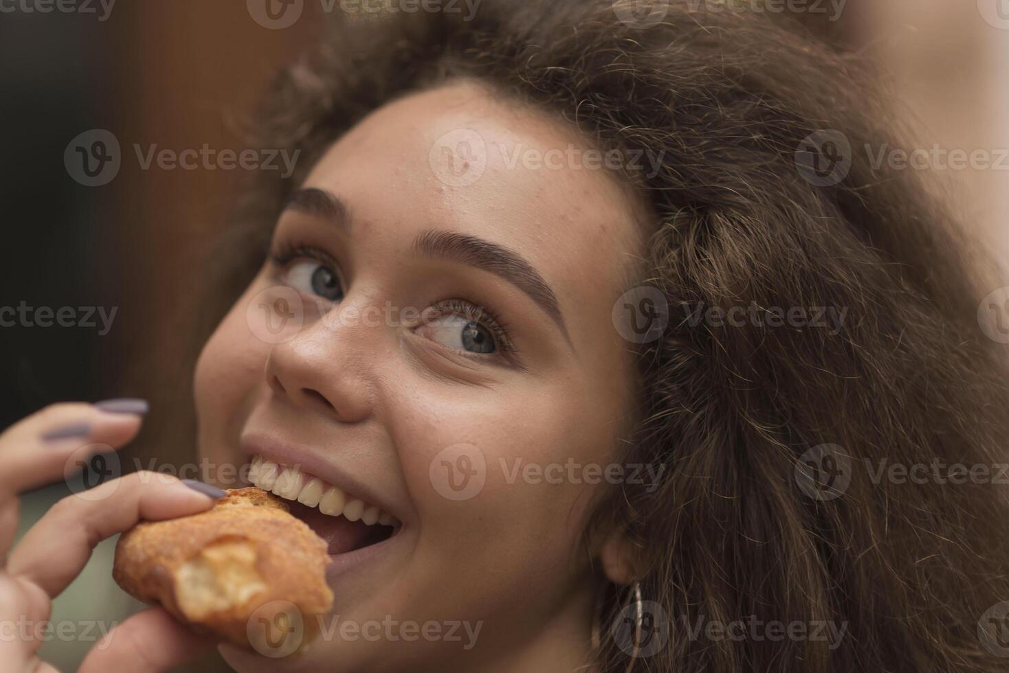A young girl eats a baguette with appetite. She has a piece of bread in her hands, she is going to eat it. She has a pleasant smile, she is looking at the camera and laughing. photo
