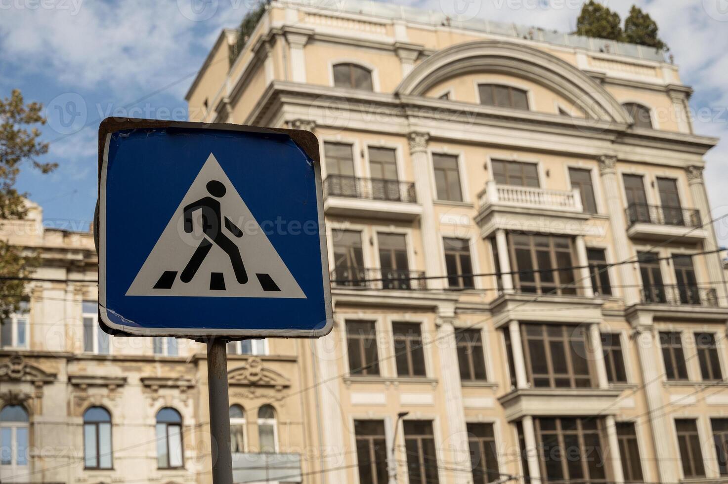 A street sign in front of a building. High quality photo. pedestrian crossing sign in the city with a building in the background. road sign in the city and a large residential building behind it photo