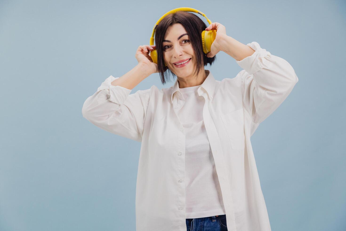 Happy mature woman listening music with yellow headphones on blue background photo