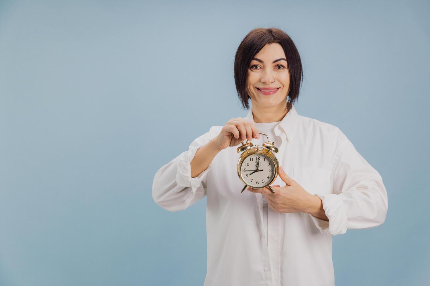 Smiling Woman Holding Alarm Clock on Blue Background photo
