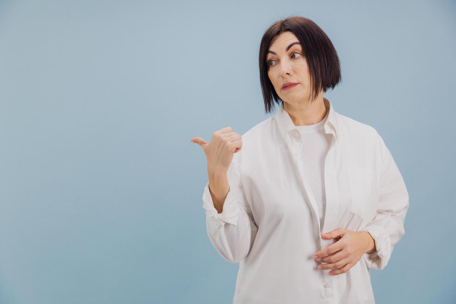Mature woman pointing with thumb aside on blue background photo