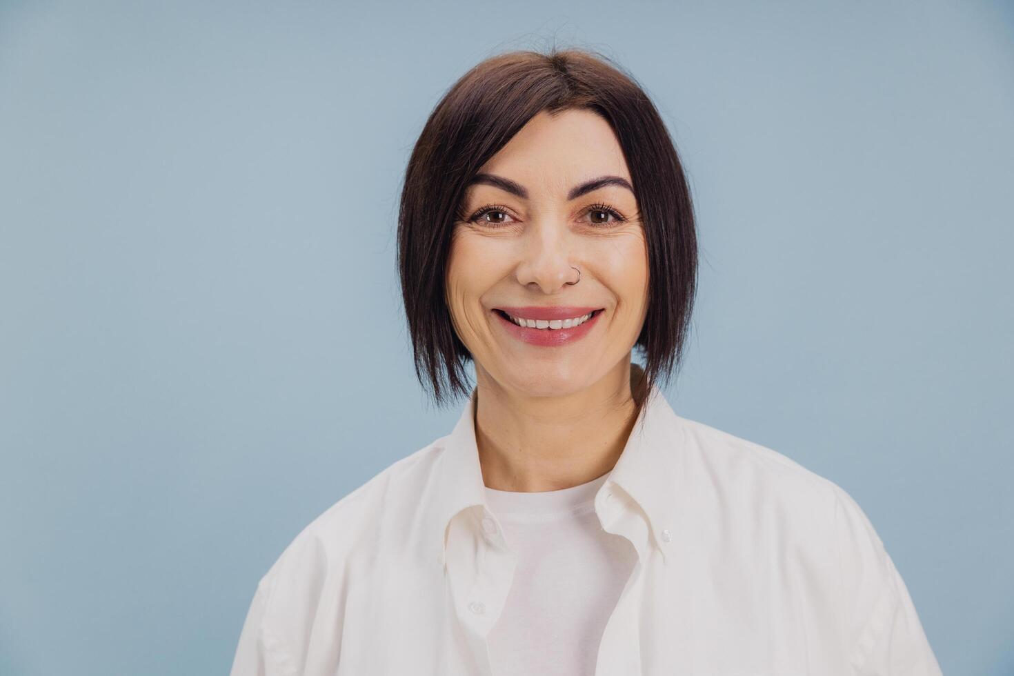 Smiling mature woman with nose piercing posing on light blue background photo