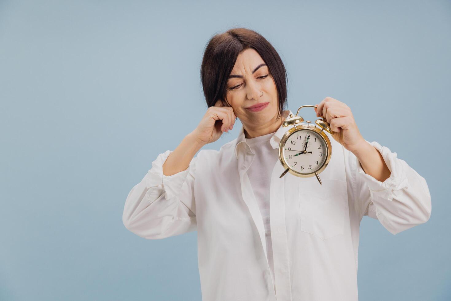 Woman covering ears showing alarm clock on blue background photo