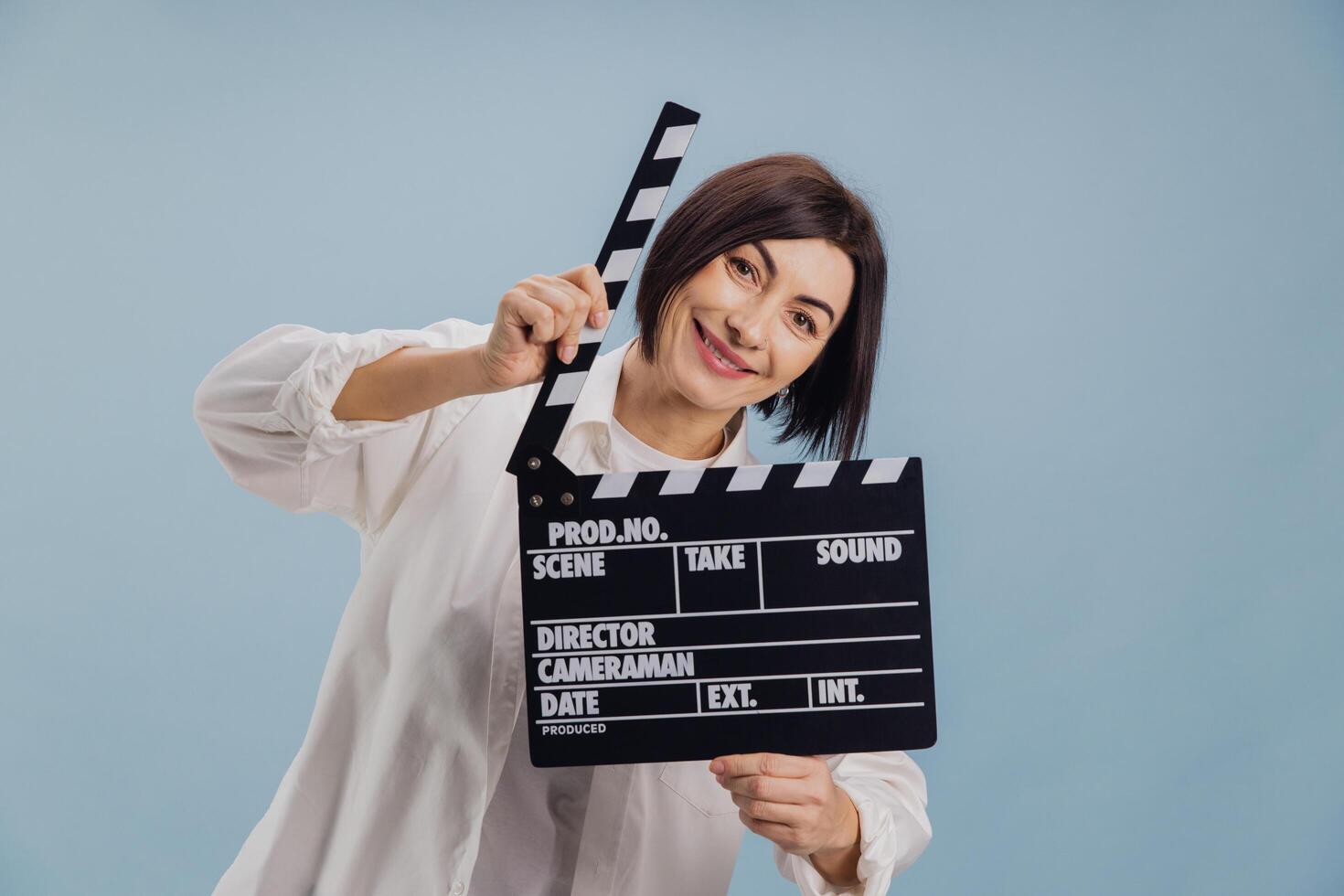 Smiling film director holding movie clapperboard on light blue background photo
