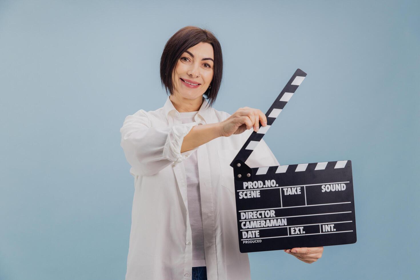 Smiling woman using movie clapperboard on blue background photo