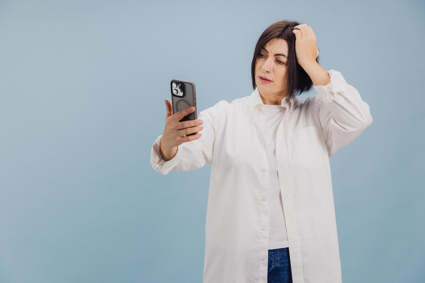 Confused mature woman scratching head while reading bad news on smartphone photo