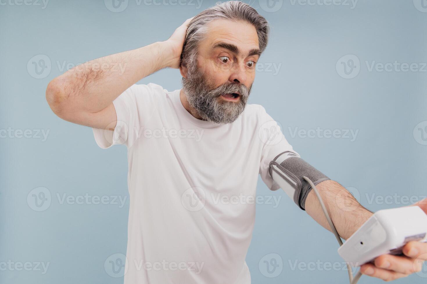 Shocked senior man checking blood pressure with digital monitor, suffering hypertension photo