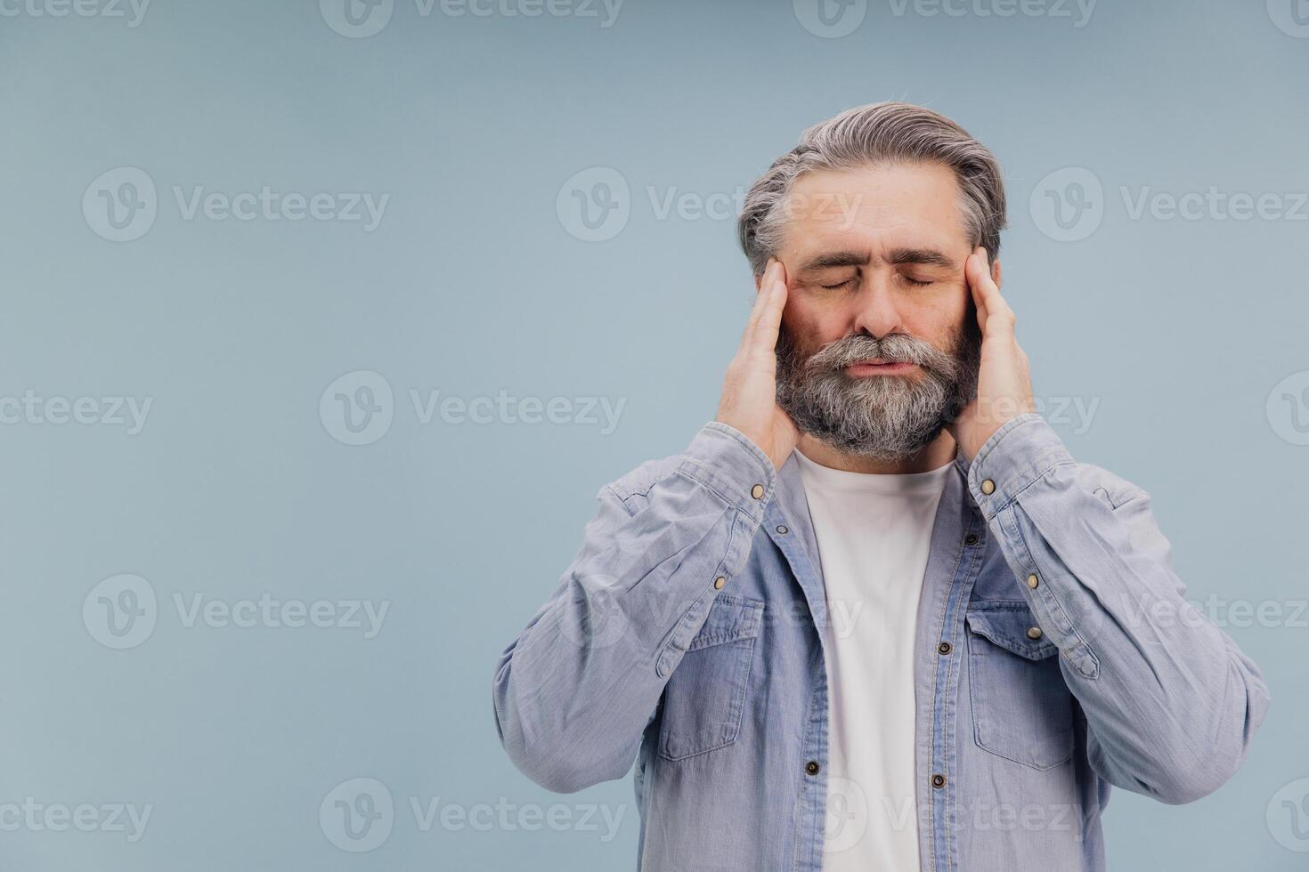Senior man suffering from headache touching temples with closed eyes on blue background photo